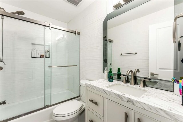 full bathroom with combined bath / shower with glass door, vanity, tile walls, and toilet