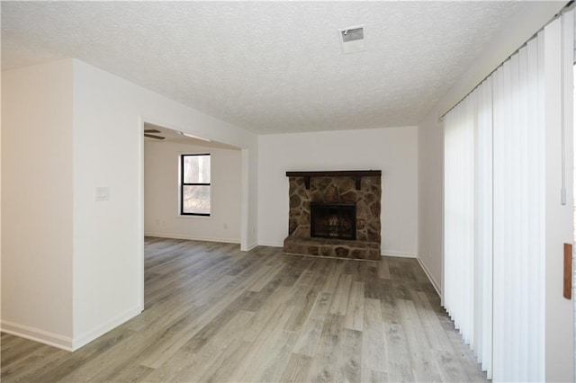 unfurnished living room with visible vents, a stone fireplace, light wood finished floors, and a textured ceiling