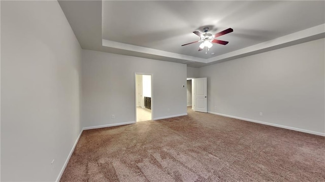 carpeted empty room with a ceiling fan, baseboards, and a tray ceiling