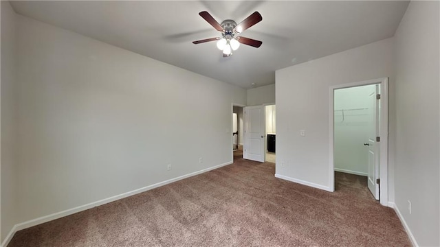 unfurnished bedroom featuring a closet, a ceiling fan, a walk in closet, dark carpet, and baseboards