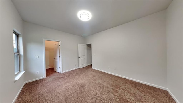 unfurnished bedroom with a walk in closet, baseboards, multiple windows, and carpet