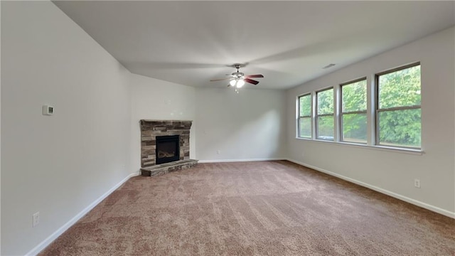 unfurnished living room featuring a ceiling fan, a stone fireplace, carpet floors, and baseboards
