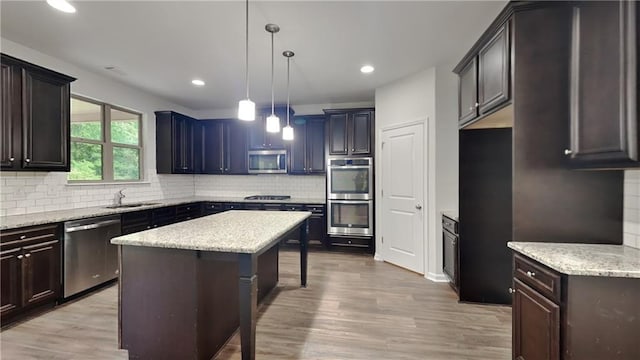kitchen with a sink, light wood-type flooring, tasteful backsplash, decorative light fixtures, and appliances with stainless steel finishes