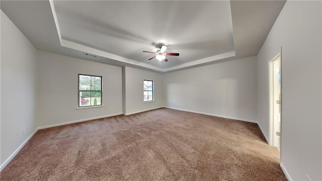 empty room featuring carpet, ceiling fan, a tray ceiling, and baseboards