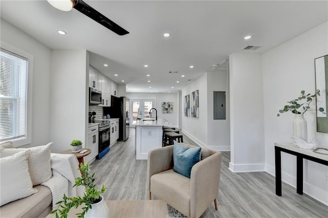 living area featuring light wood-style flooring, recessed lighting, visible vents, baseboards, and electric panel