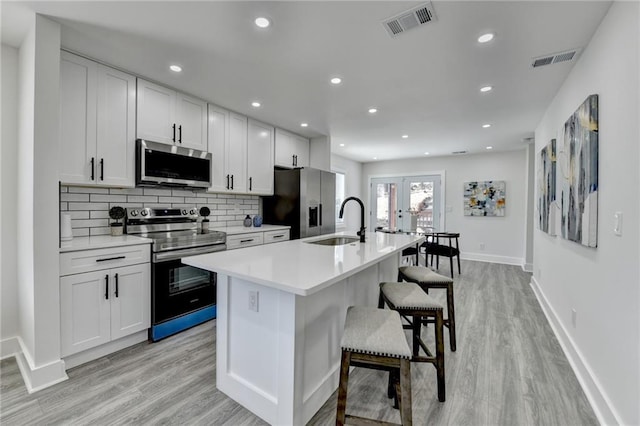 kitchen featuring a center island with sink, white cabinets, stainless steel appliances, light countertops, and french doors