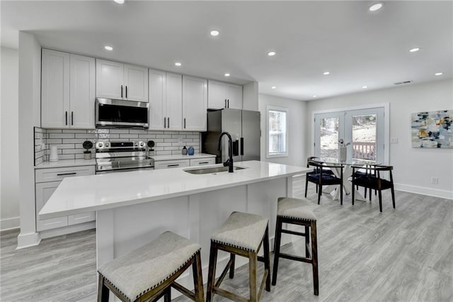 kitchen with a center island with sink, stainless steel appliances, light countertops, white cabinets, and a kitchen breakfast bar