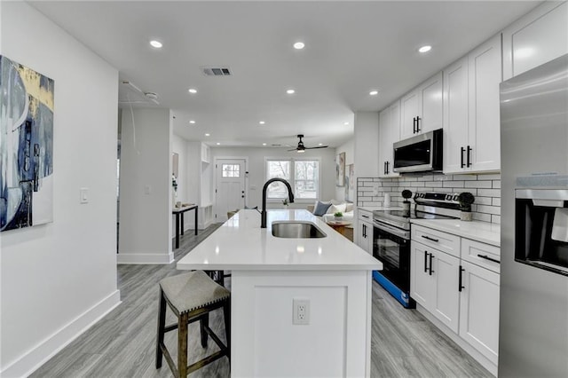 kitchen featuring stainless steel appliances, a sink, white cabinetry, light countertops, and a center island with sink