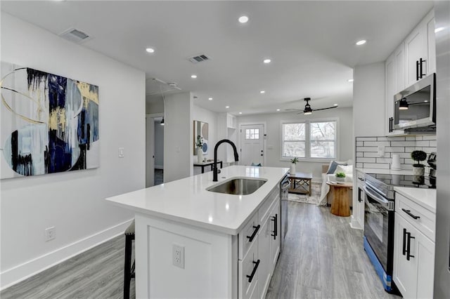 kitchen featuring stainless steel appliances, visible vents, white cabinetry, light countertops, and an island with sink