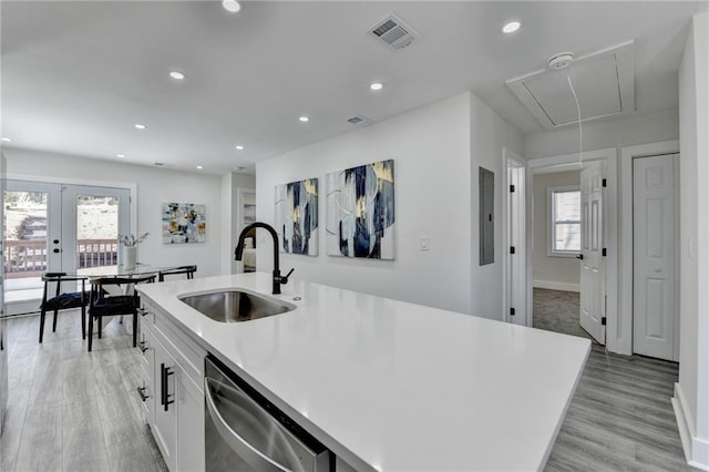 kitchen with a sink, white cabinetry, light countertops, stainless steel dishwasher, and a center island with sink