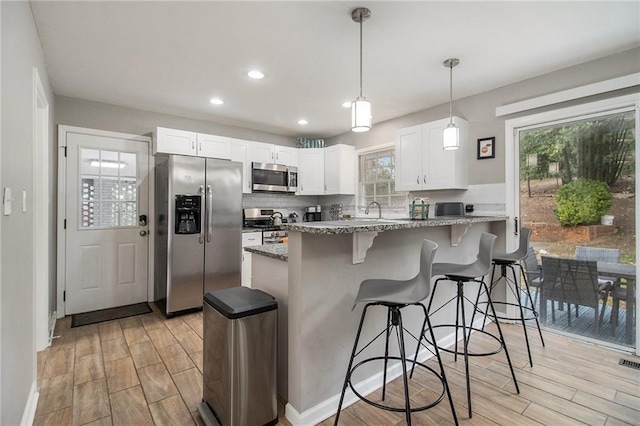 kitchen with white cabinets, appliances with stainless steel finishes, stone counters, and a breakfast bar area