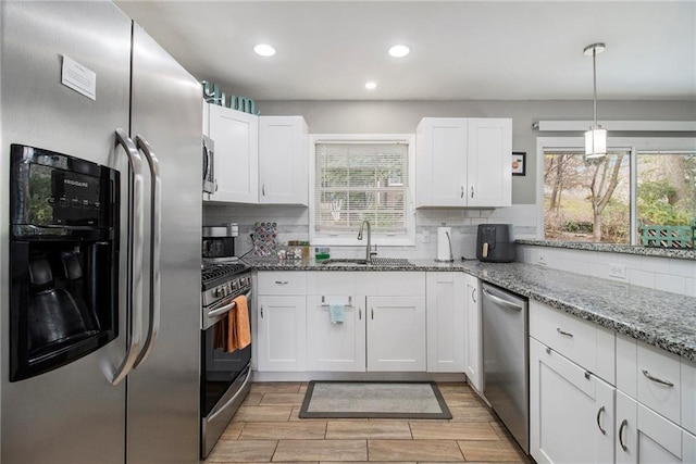 kitchen featuring backsplash, white cabinets, hanging light fixtures, light stone countertops, and stainless steel appliances