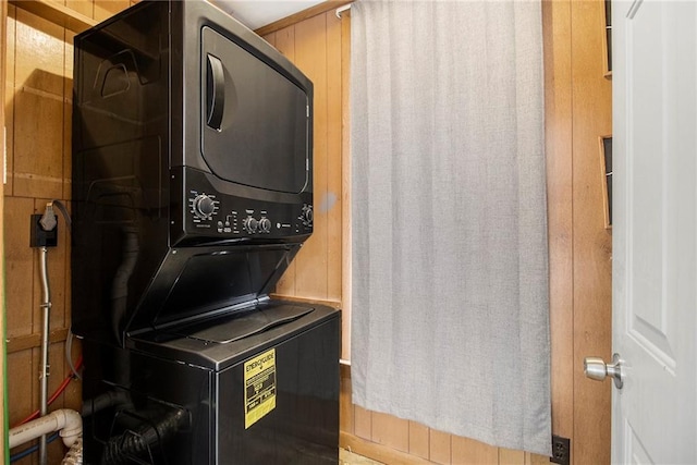 laundry area with stacked washer / drying machine and wood walls