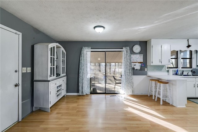 kitchen with white cabinetry, a kitchen bar, kitchen peninsula, decorative backsplash, and a textured ceiling