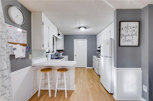 kitchen with white cabinetry, a kitchen bar, kitchen peninsula, backsplash, and white appliances