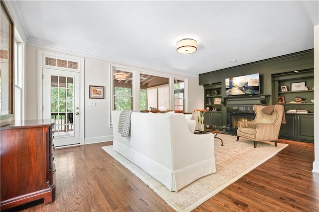 living room featuring a fireplace, hardwood / wood-style flooring, crown molding, and built in shelves