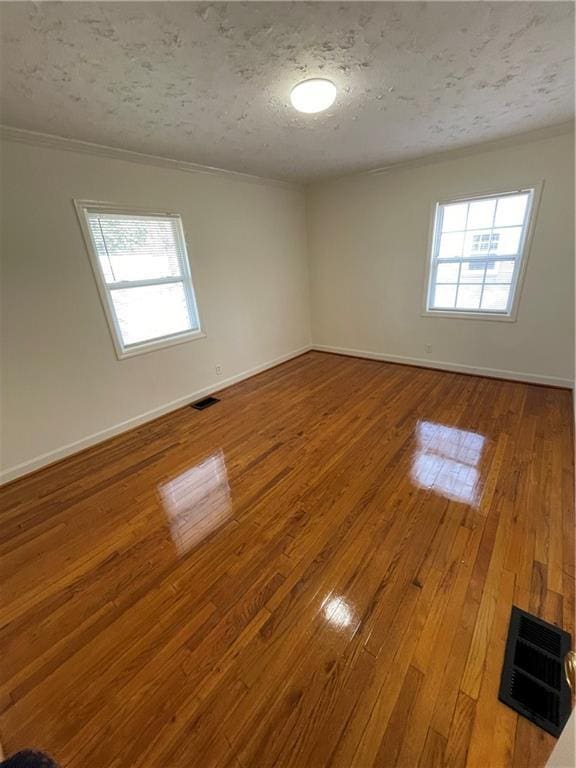 unfurnished room featuring plenty of natural light, visible vents, and hardwood / wood-style floors