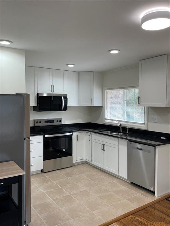 kitchen featuring appliances with stainless steel finishes, dark countertops, a sink, and white cabinetry