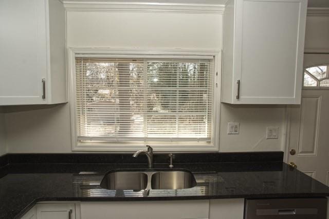 kitchen with dark stone counters, white cabinets, a sink, and dishwashing machine