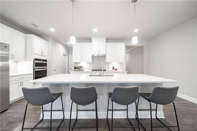 kitchen featuring stainless steel appliances, pendant lighting, white cabinets, and a center island with sink