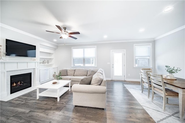 living room featuring ceiling fan, dark hardwood / wood-style floors, a premium fireplace, built in features, and ornamental molding