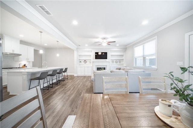 dining space with light hardwood / wood-style floors, ceiling fan, built in features, ornamental molding, and sink