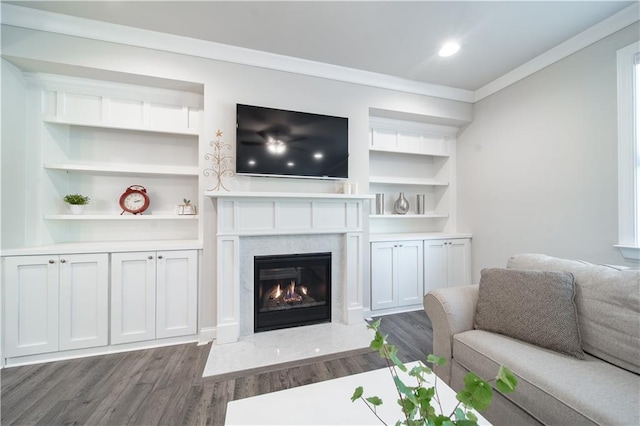 living room with hardwood / wood-style flooring, a high end fireplace, built in features, and ornamental molding