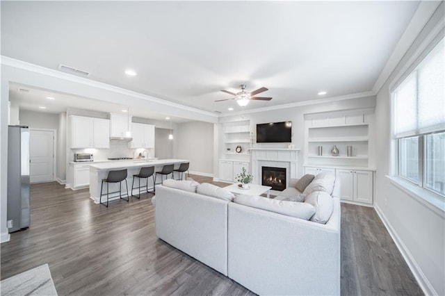 living room featuring dark wood-type flooring, ornamental molding, built in features, and ceiling fan