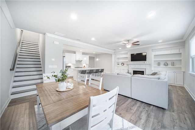 dining room with ceiling fan, built in features, crown molding, and light hardwood / wood-style flooring