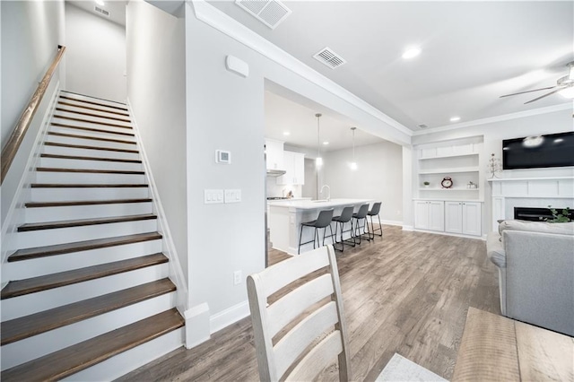 interior space featuring ceiling fan, sink, hardwood / wood-style flooring, ornamental molding, and built in shelves