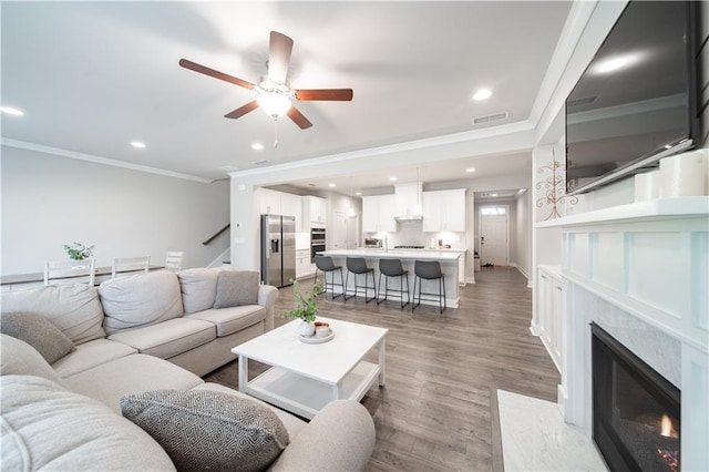 living room featuring ceiling fan, a high end fireplace, crown molding, and hardwood / wood-style flooring