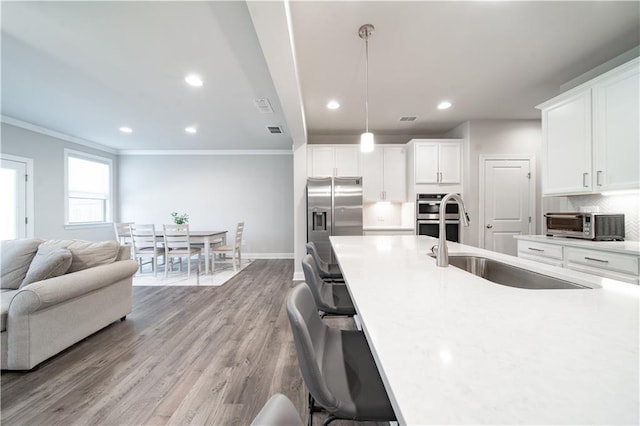 kitchen with stainless steel appliances, backsplash, light wood-type flooring, pendant lighting, and white cabinets