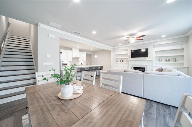 dining space with ceiling fan, built in features, dark hardwood / wood-style flooring, and ornamental molding