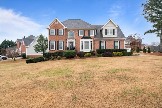 view of front of house with brick siding, a front yard, and a shingled roof