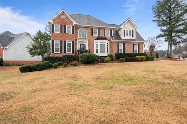 colonial home featuring brick siding, a front yard, and roof with shingles