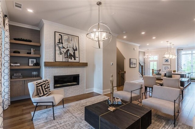 living room featuring a notable chandelier, a fireplace, hardwood / wood-style flooring, ornamental molding, and built in features