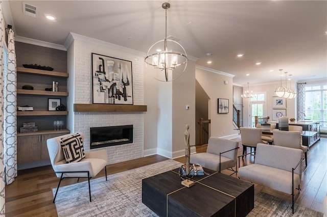 living room featuring hardwood / wood-style flooring, ornamental molding, a brick fireplace, and a notable chandelier