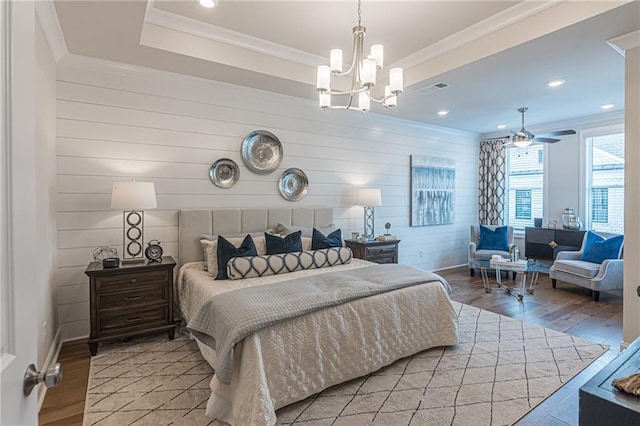 bedroom featuring a chandelier, a raised ceiling, light wood-type flooring, and ornamental molding