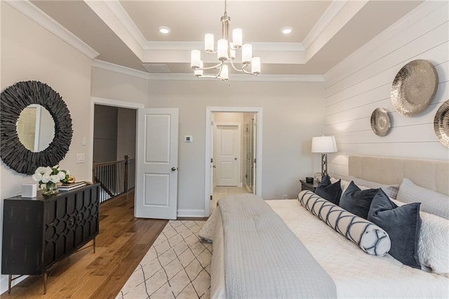 bedroom featuring an inviting chandelier, ornamental molding, hardwood / wood-style floors, and a tray ceiling