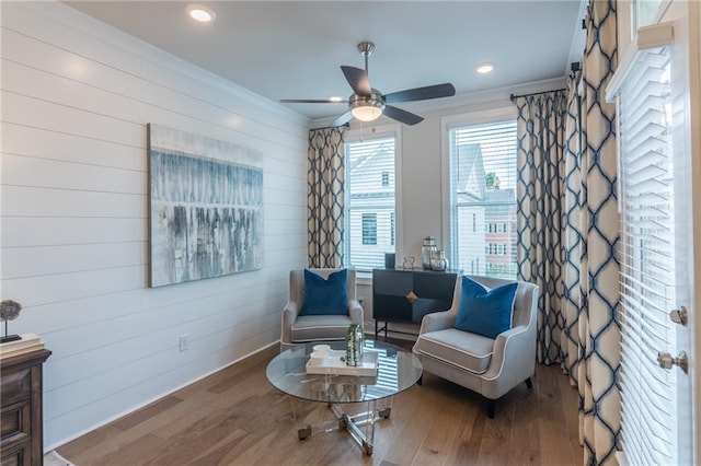 sitting room with wooden walls, ceiling fan, and hardwood / wood-style floors