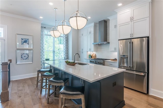 kitchen with sink, a kitchen island with sink, light wood-type flooring, high quality fridge, and wall chimney exhaust hood