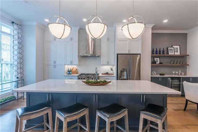 kitchen featuring high end fridge, pendant lighting, crown molding, and an island with sink