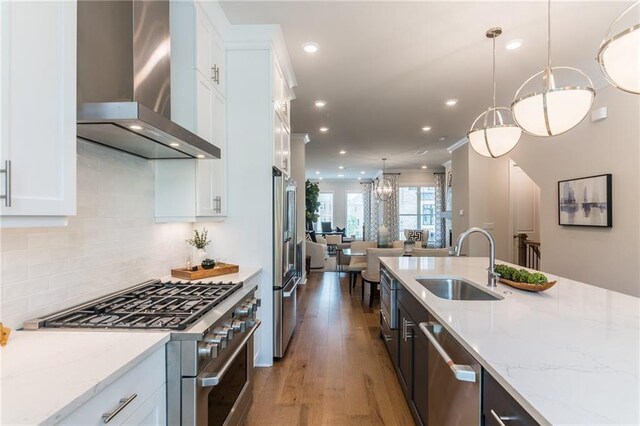 kitchen with premium appliances, white cabinetry, wall chimney exhaust hood, pendant lighting, and sink