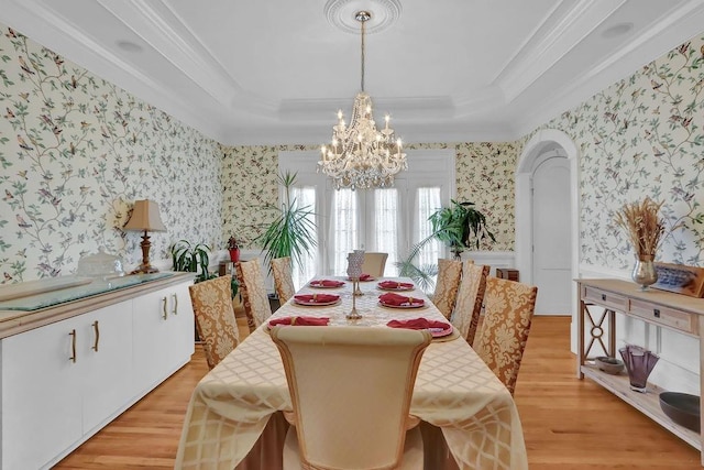 dining space featuring an inviting chandelier, crown molding, light wood-type flooring, and a raised ceiling