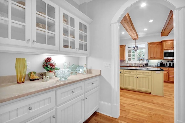 kitchen featuring beamed ceiling, hanging light fixtures, light hardwood / wood-style floors, and light stone counters