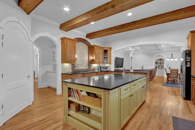 kitchen with decorative backsplash, beamed ceiling, a center island with sink, light hardwood / wood-style floors, and stainless steel refrigerator