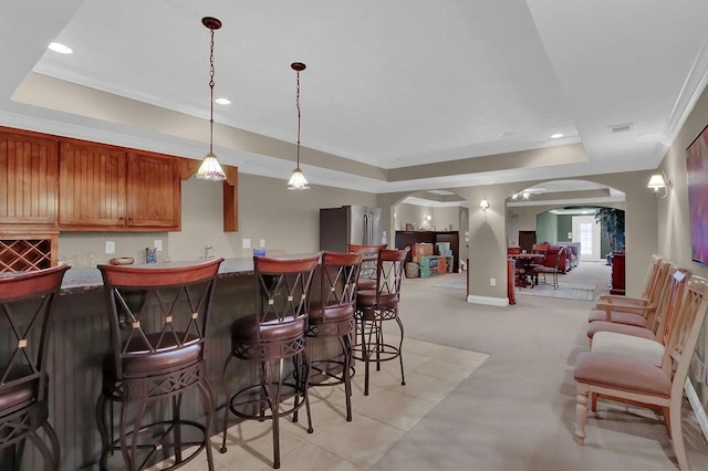 kitchen with stainless steel fridge, hanging light fixtures, light colored carpet, and a raised ceiling