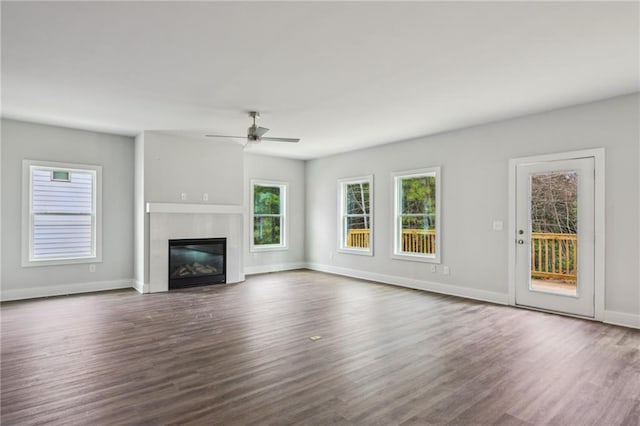 unfurnished living room featuring dark wood-style floors, a glass covered fireplace, a ceiling fan, and baseboards