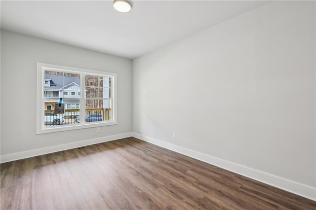 empty room with visible vents, dark wood-style floors, and baseboards