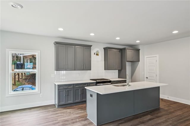 kitchen with a sink, backsplash, dark wood-type flooring, stainless steel gas stove, and a kitchen island with sink